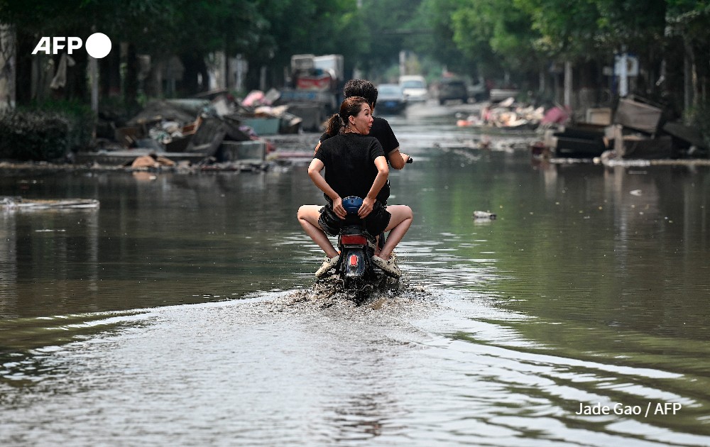 Local residents ride a scooter on a flooded street